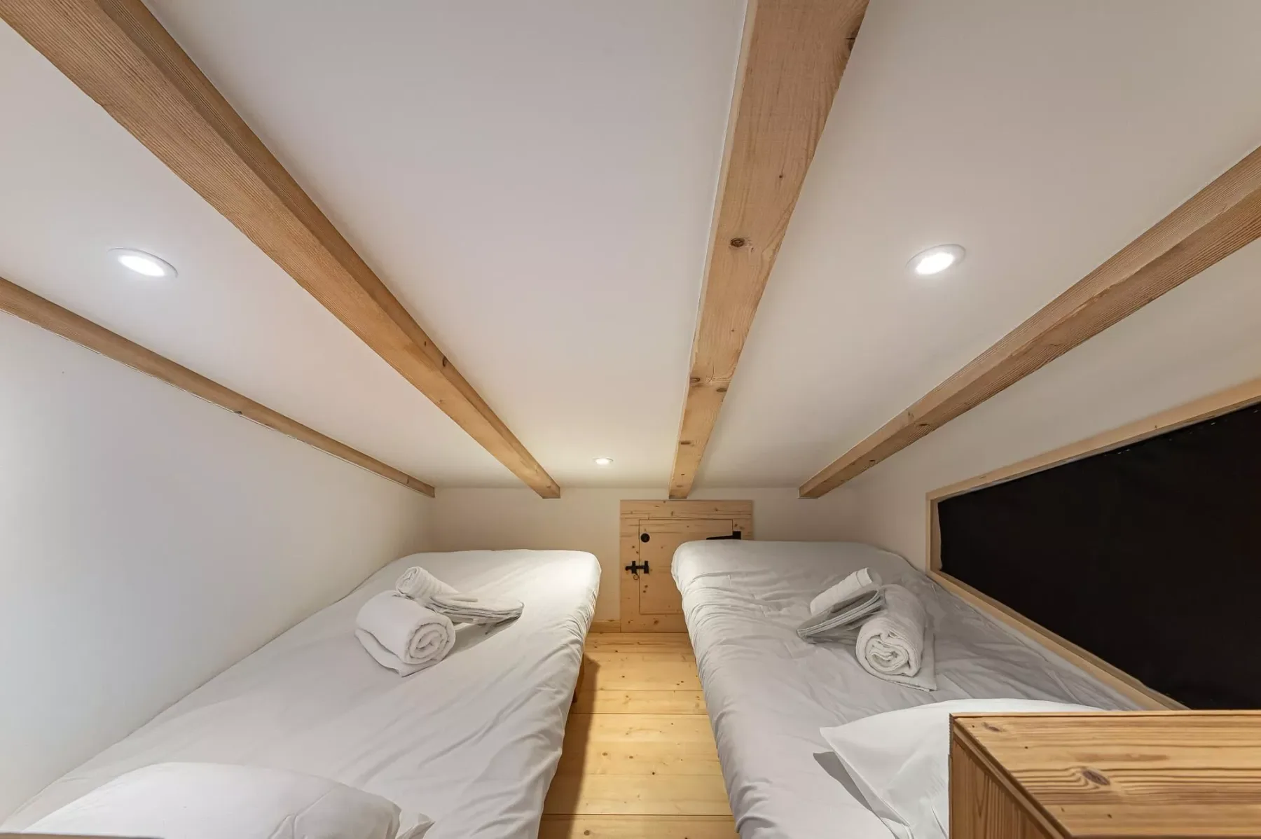 Una zona compacta para dormir con dos camas bajo vigas de madera vistas.