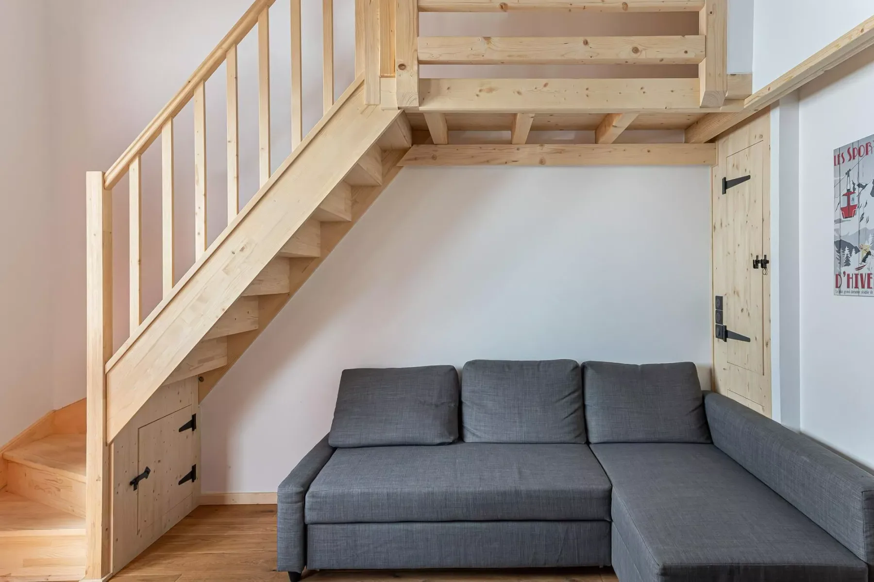 Una sala de estar con asientos grises bajo una escalera de madera.