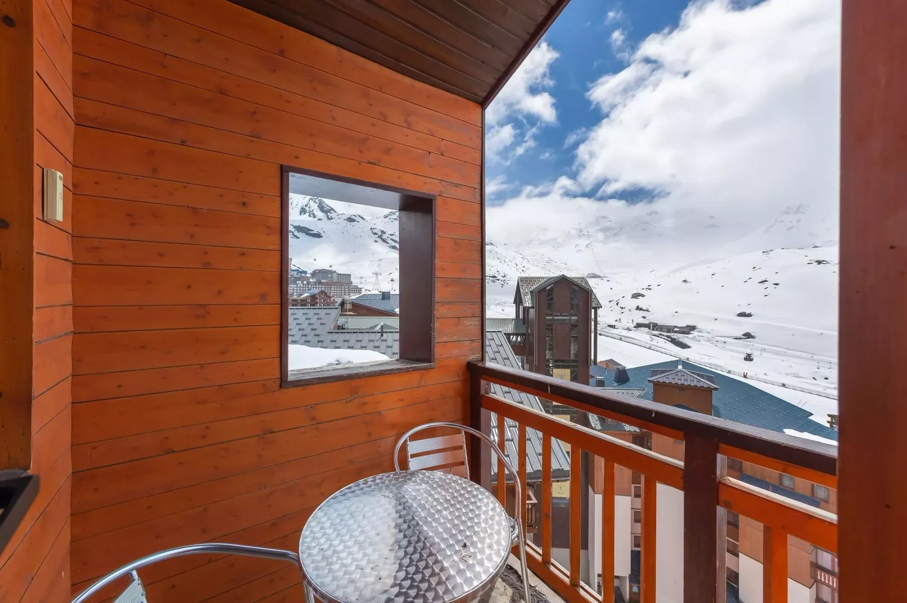 A wooden balcony with a round table overlooks a snowy mountain landscape.