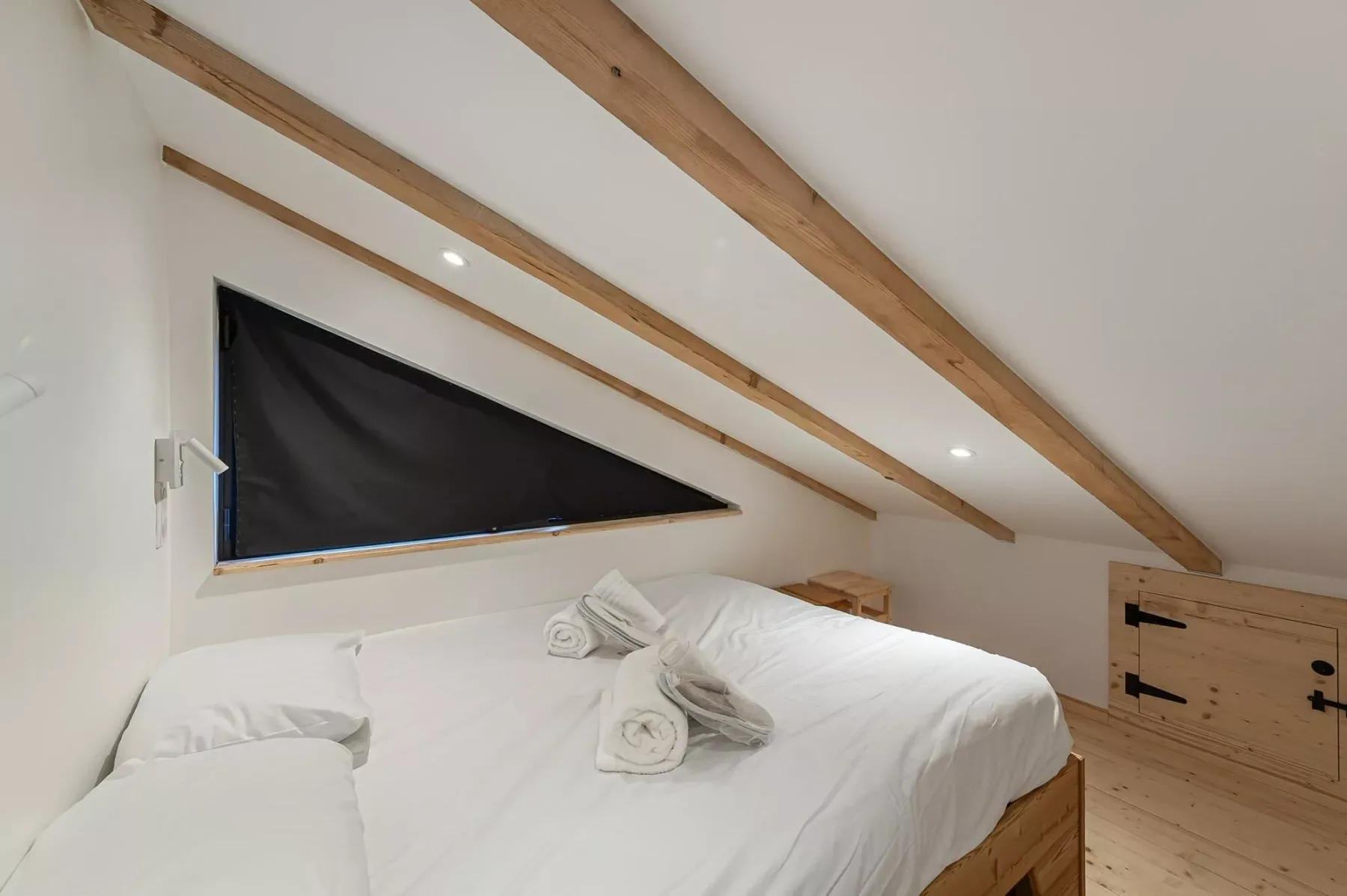 Un dormitorio con una cama bajo un techo inclinado con vigas de madera a la vista.
