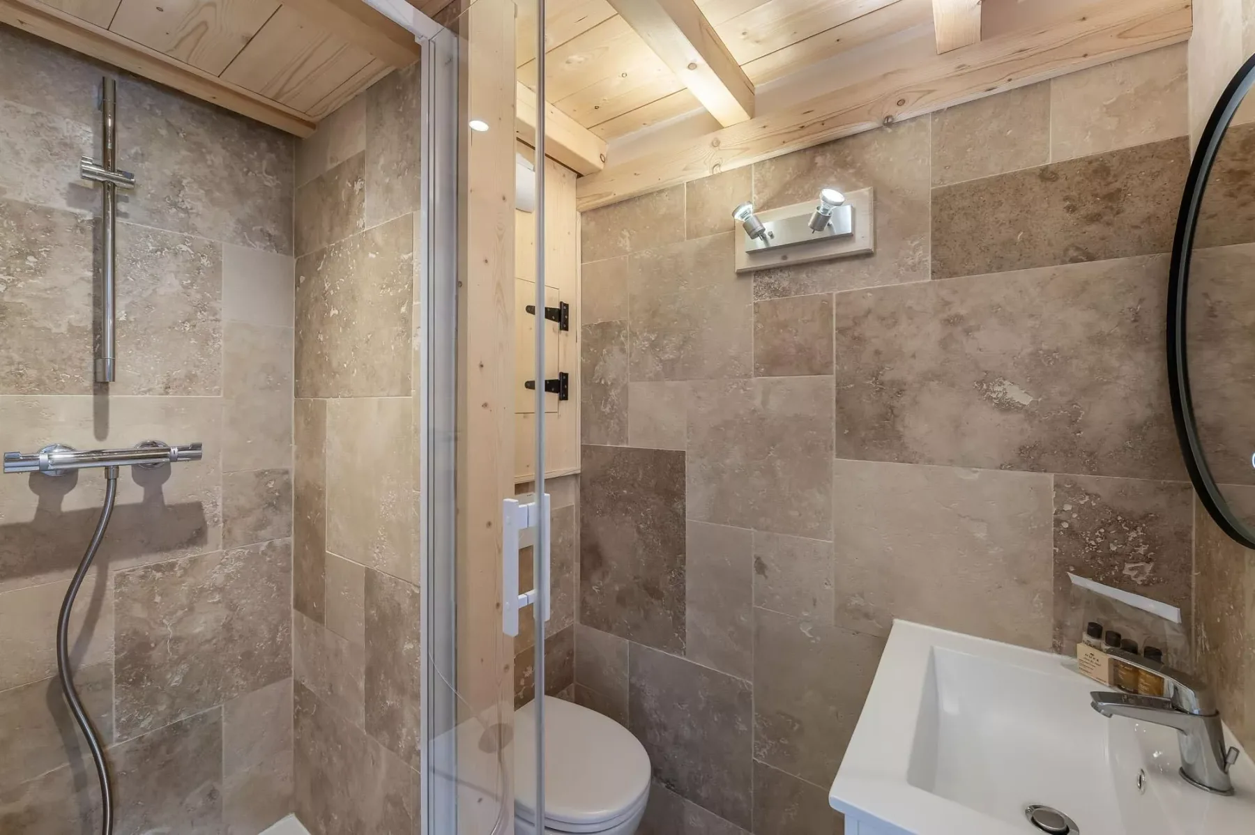 Un baño con azulejos, ducha, inodoro y lavabo bajo un techo de madera.
