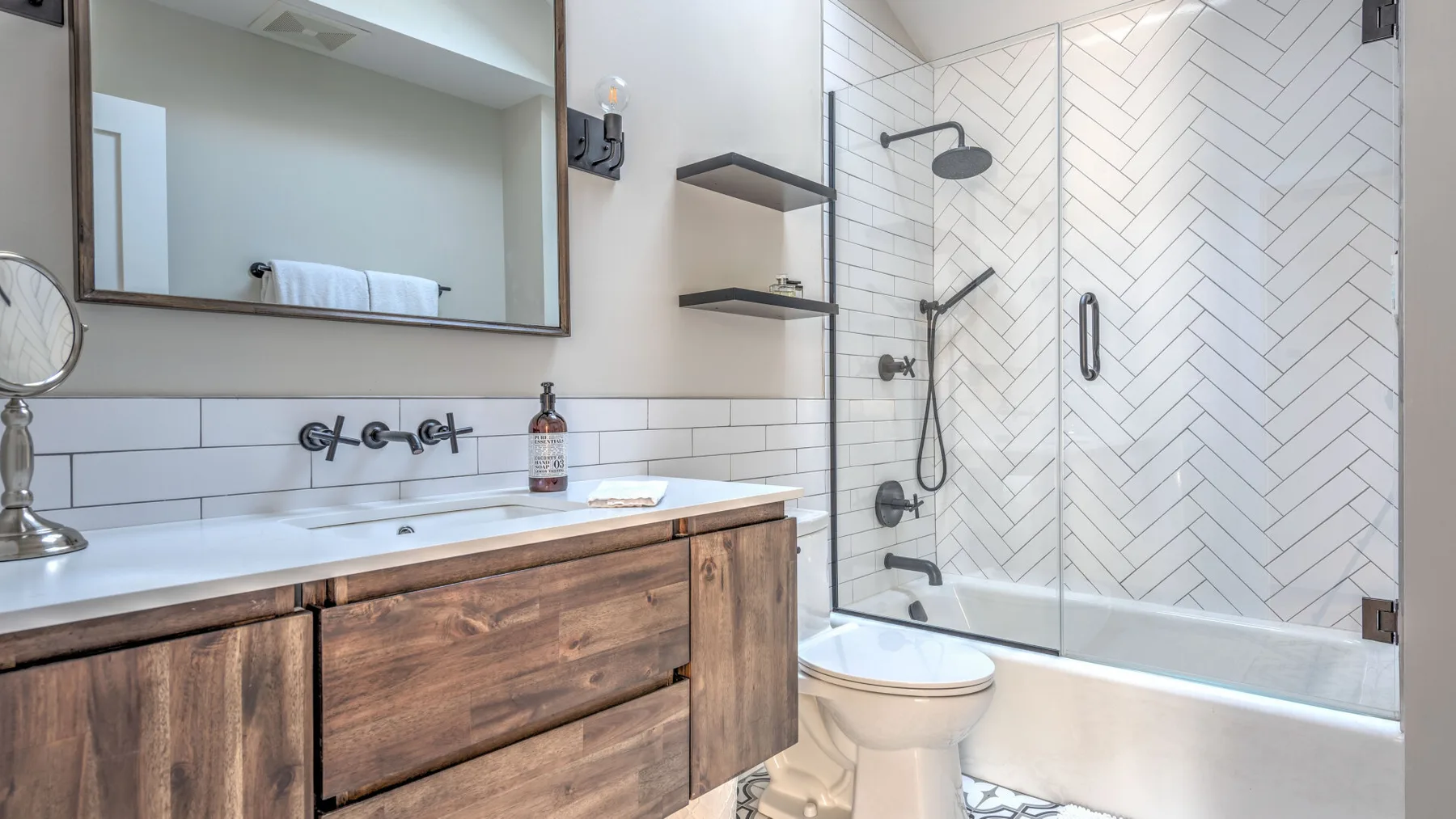 A bathroom with a wood vanity, white sink, and tiled shower.