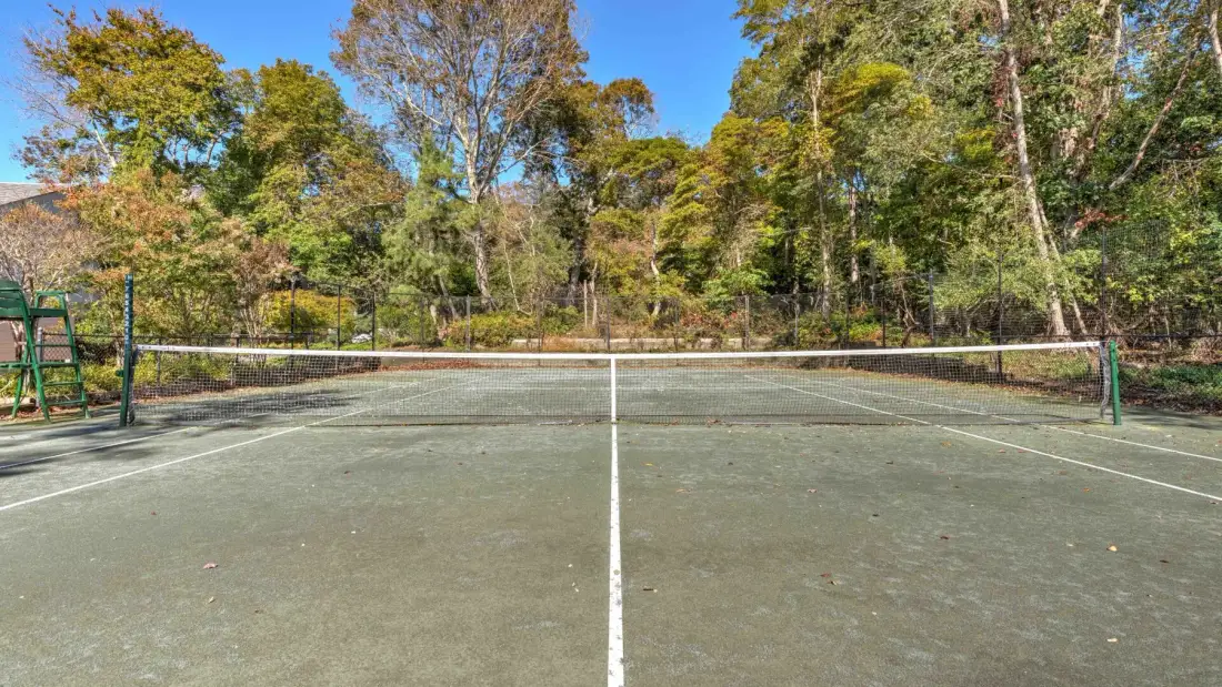 An outdoor tennis court with a net and trees surrounding it.