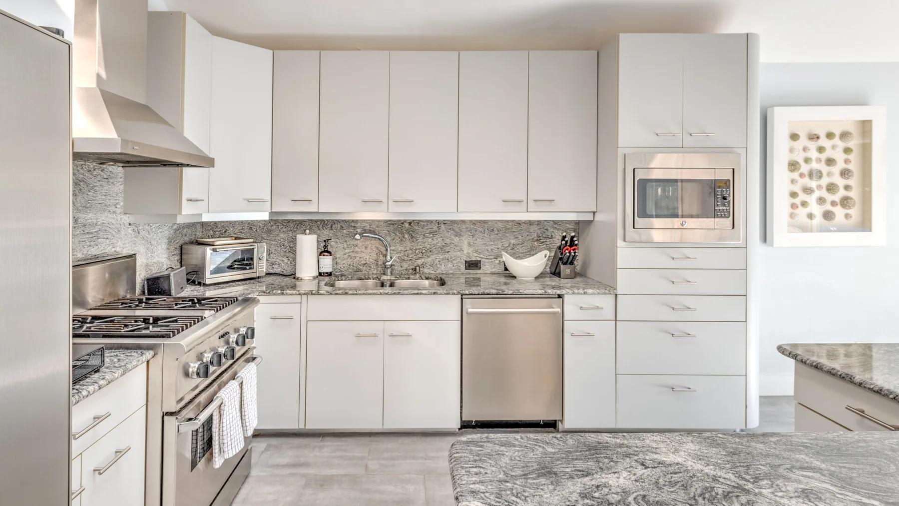 A bright modern kitchen with white cabinets, stainless steel appliances, and a stone backsplash.