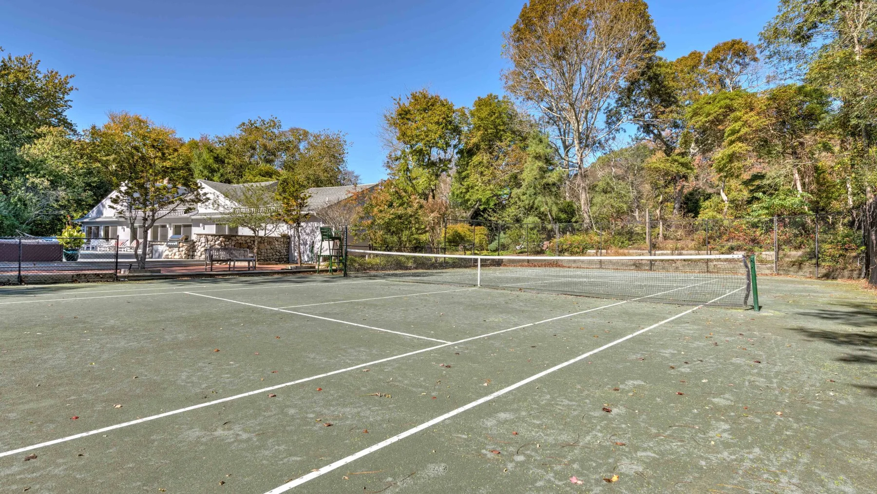 An outdoor tennis court with a net, surrounded by trees.