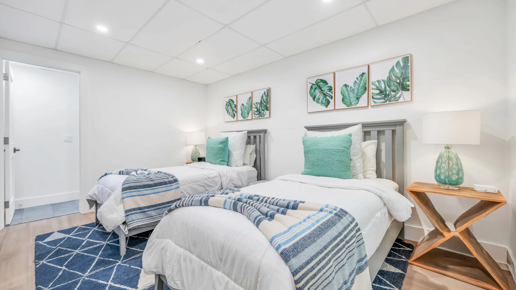 A bedroom with two beds, blue-and-white bedding, and botanical wall art.
