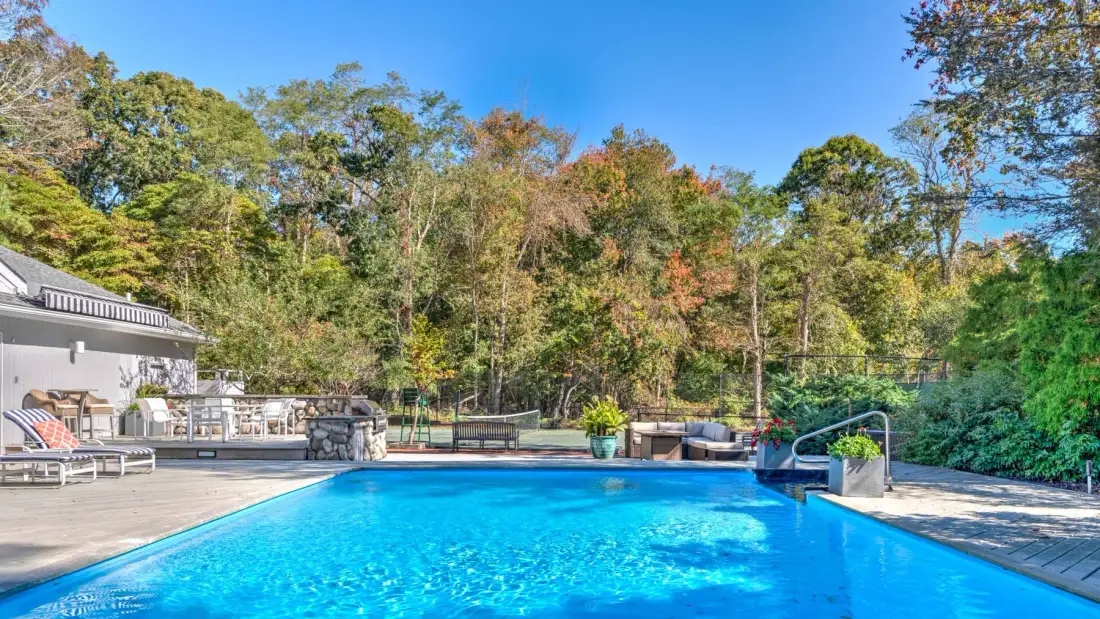 An outdoor swimming pool sits beside a patio, with trees surrounding the area.