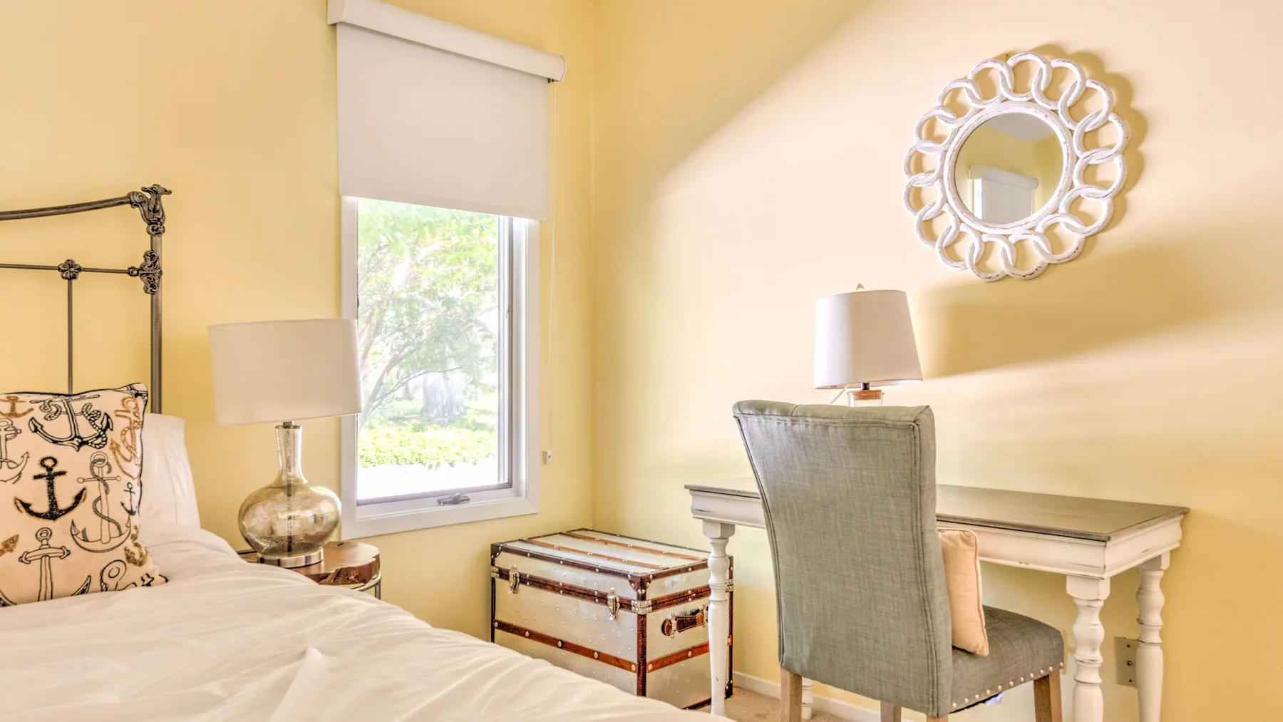 A bright bedroom with a bed, a desk, and a window overlooking greenery.