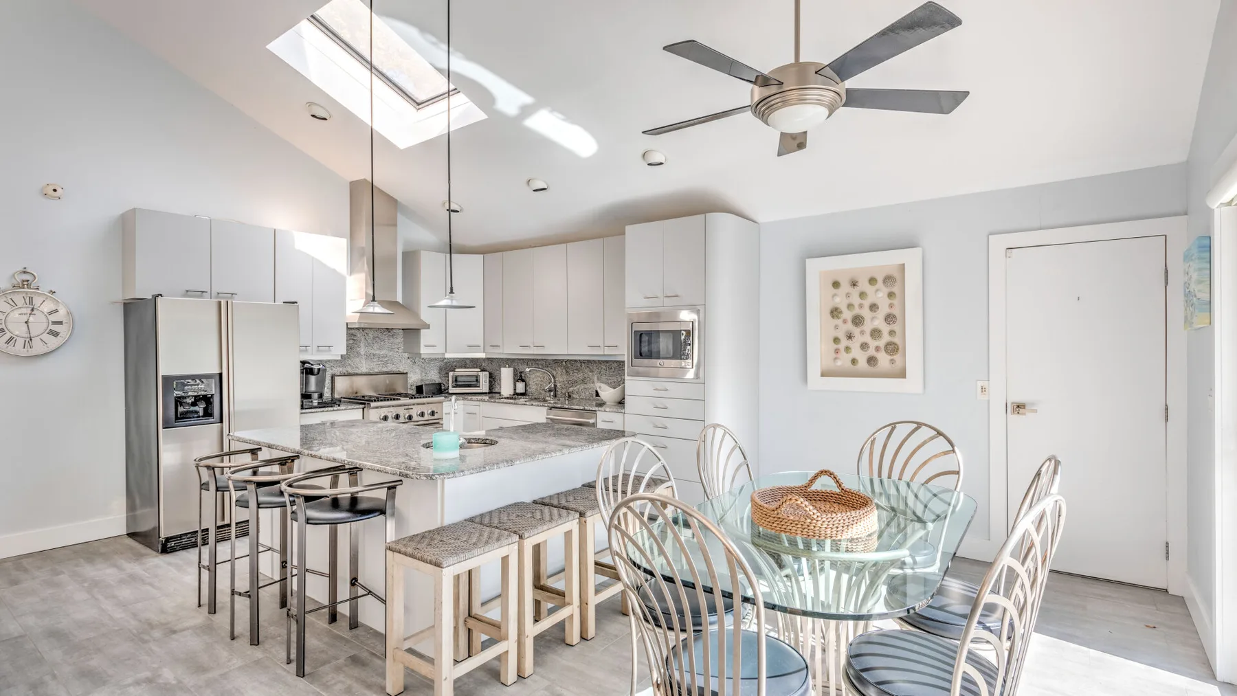 A bright kitchen and dining area with white cabinets, an island, and a glass table.