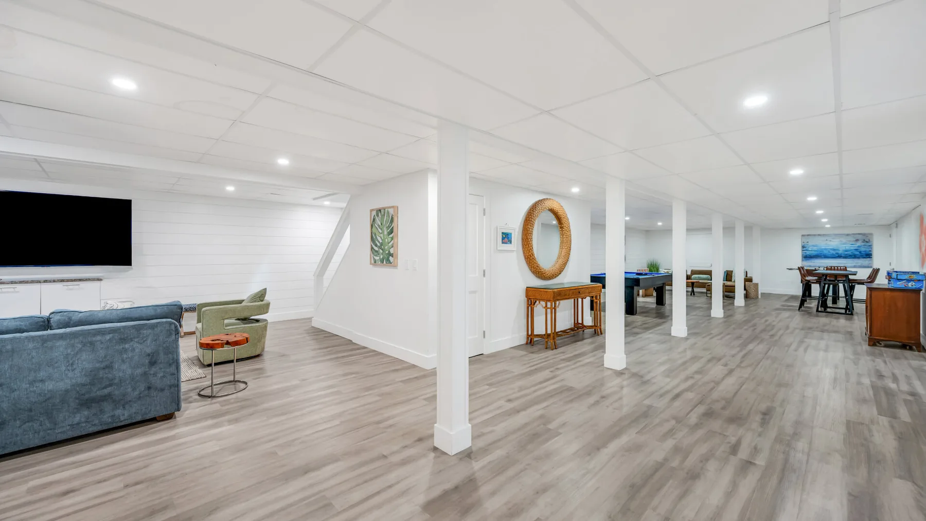 A spacious basement recreation room with seating, a television, and a game table.