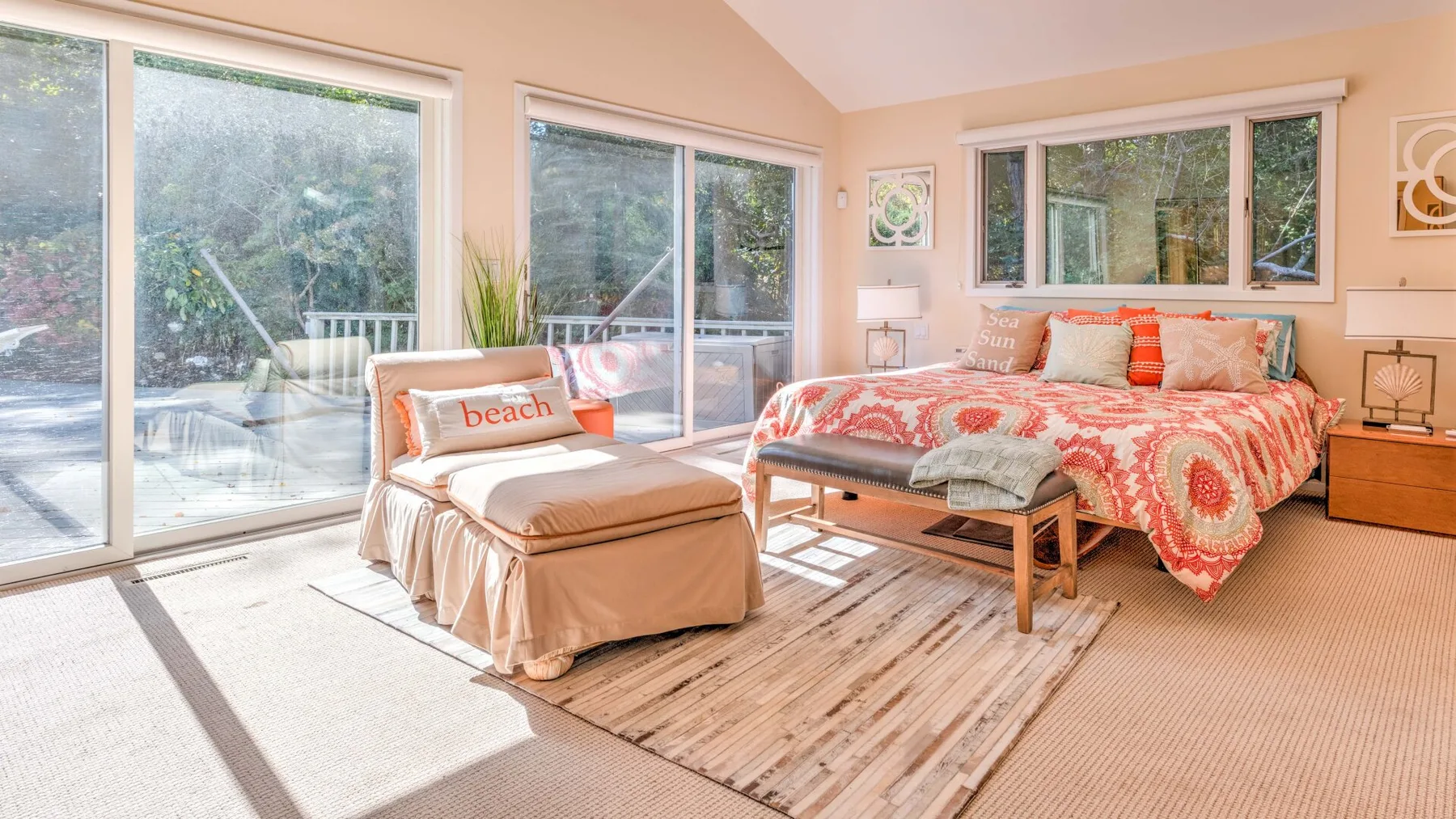 A bright bedroom with a bed, a chaise lounge, and large windows.