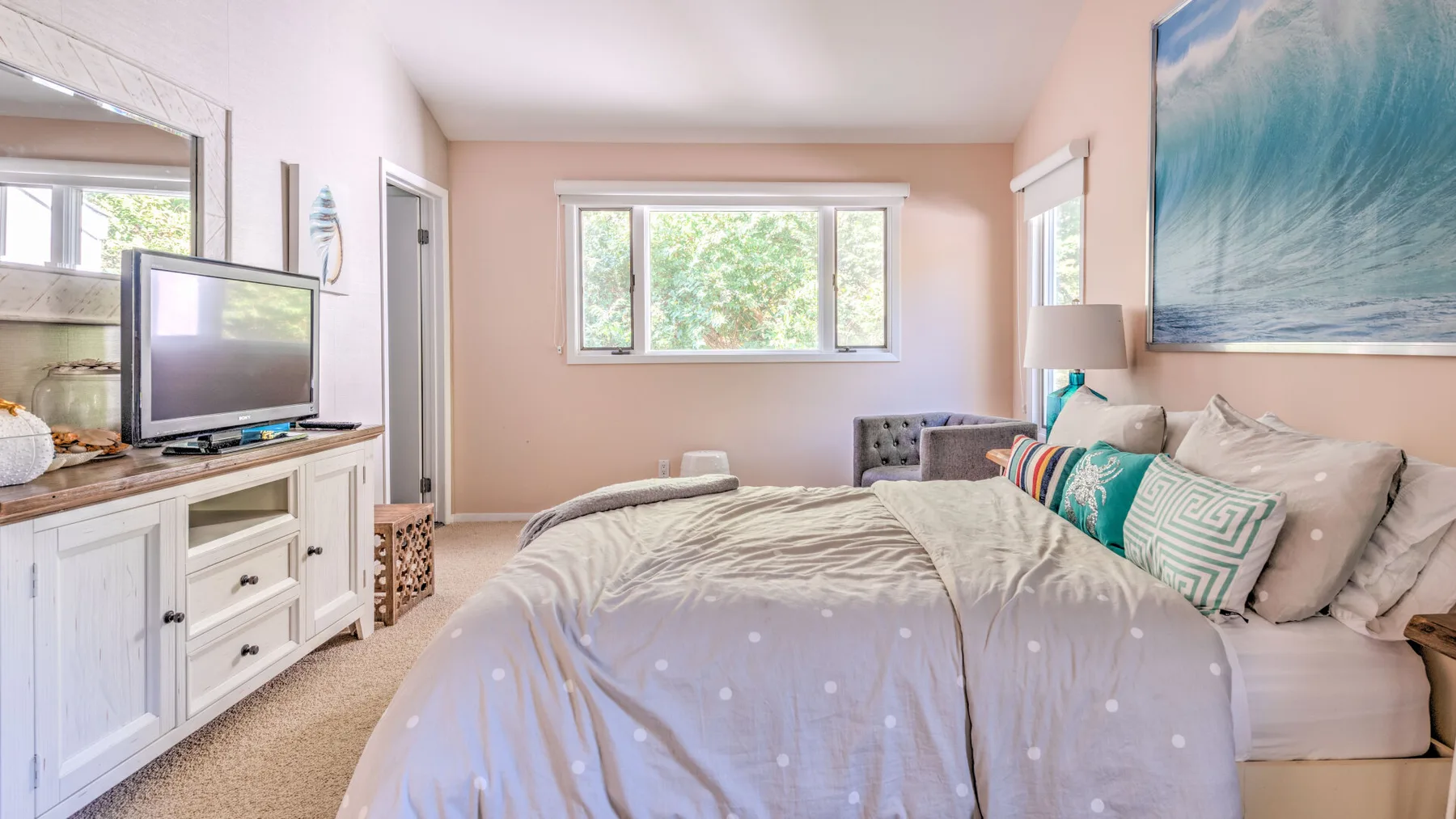 A bright bedroom with a neatly made bed and a television on a dresser.