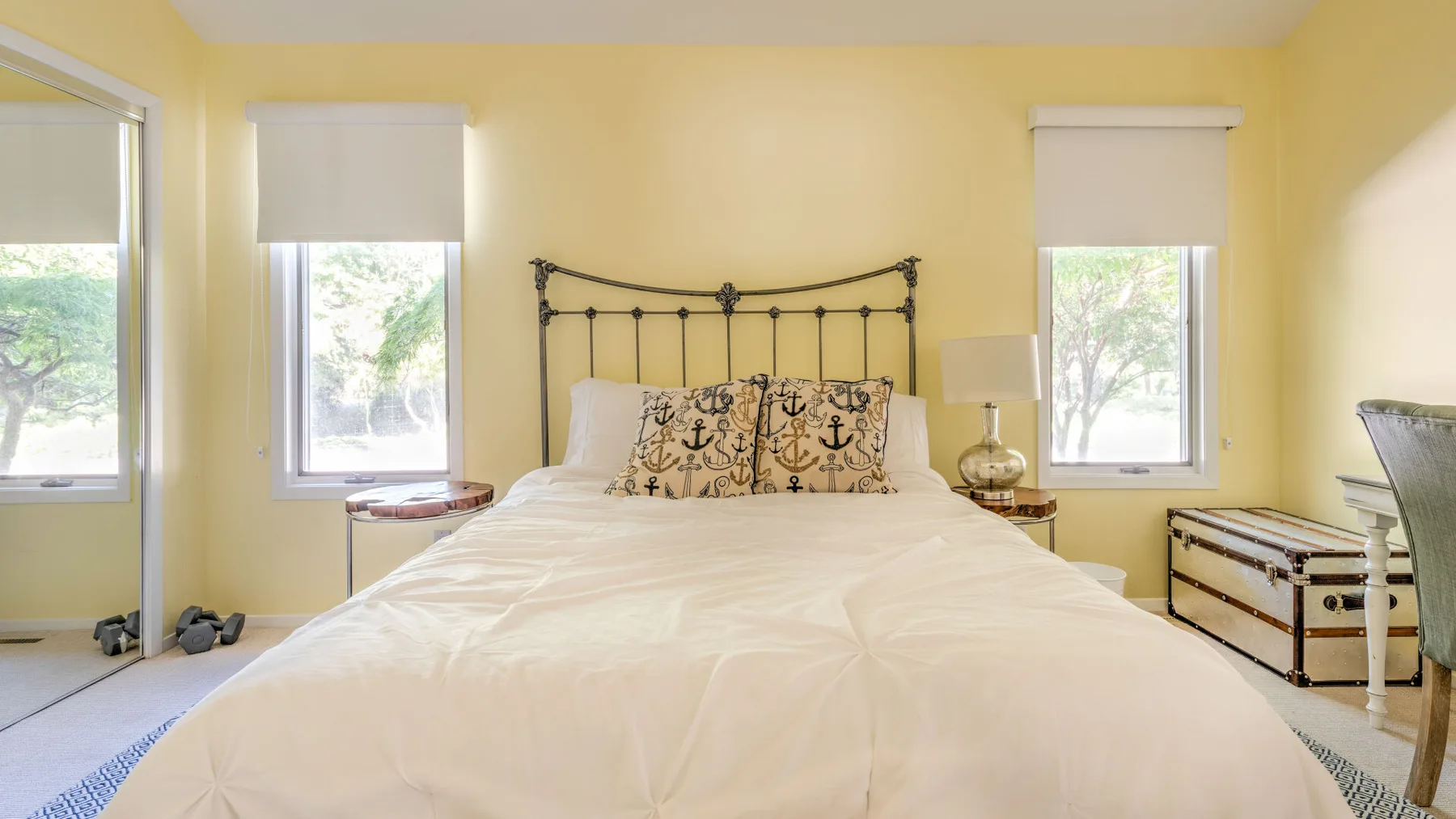 A bright bedroom with a bed, patterned pillows, and windows.