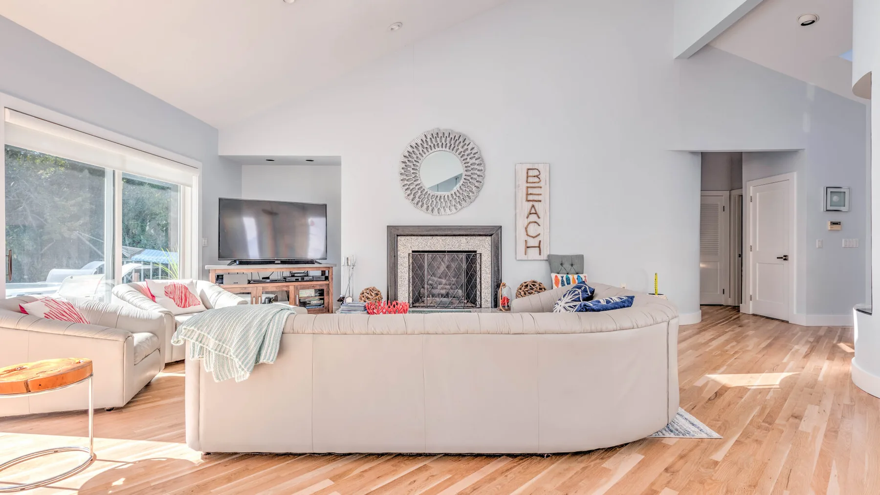 A bright living room with curved seating facing a fireplace and television.