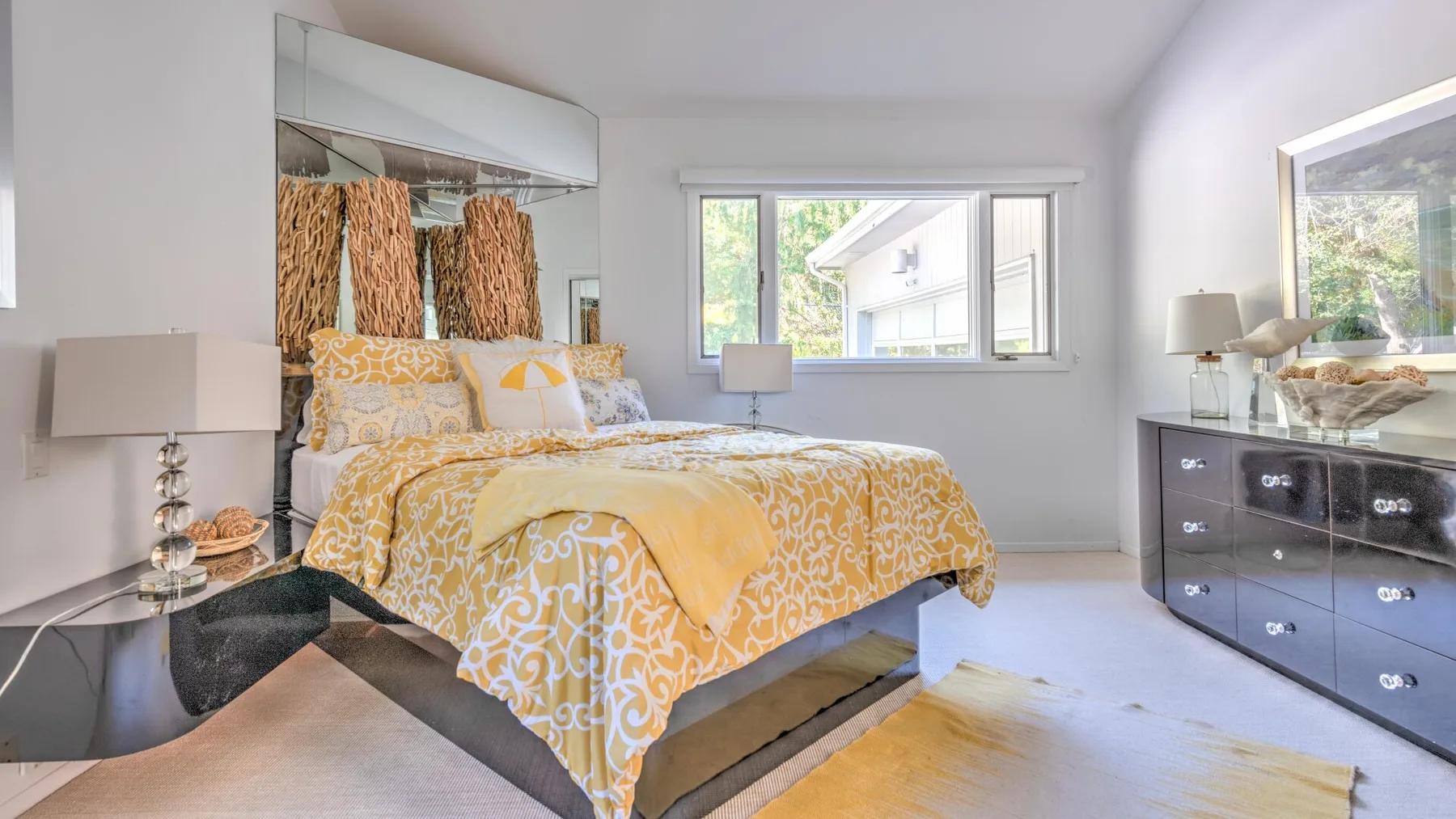 A bedroom with a bed dressed in yellow patterned bedding and windows.