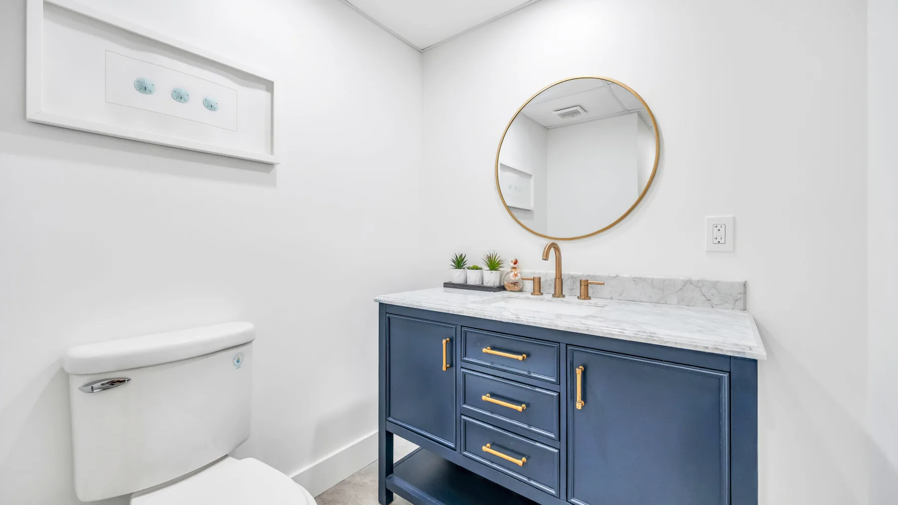 A bathroom vanity with blue cabinetry, a white countertop, and a round mirror.