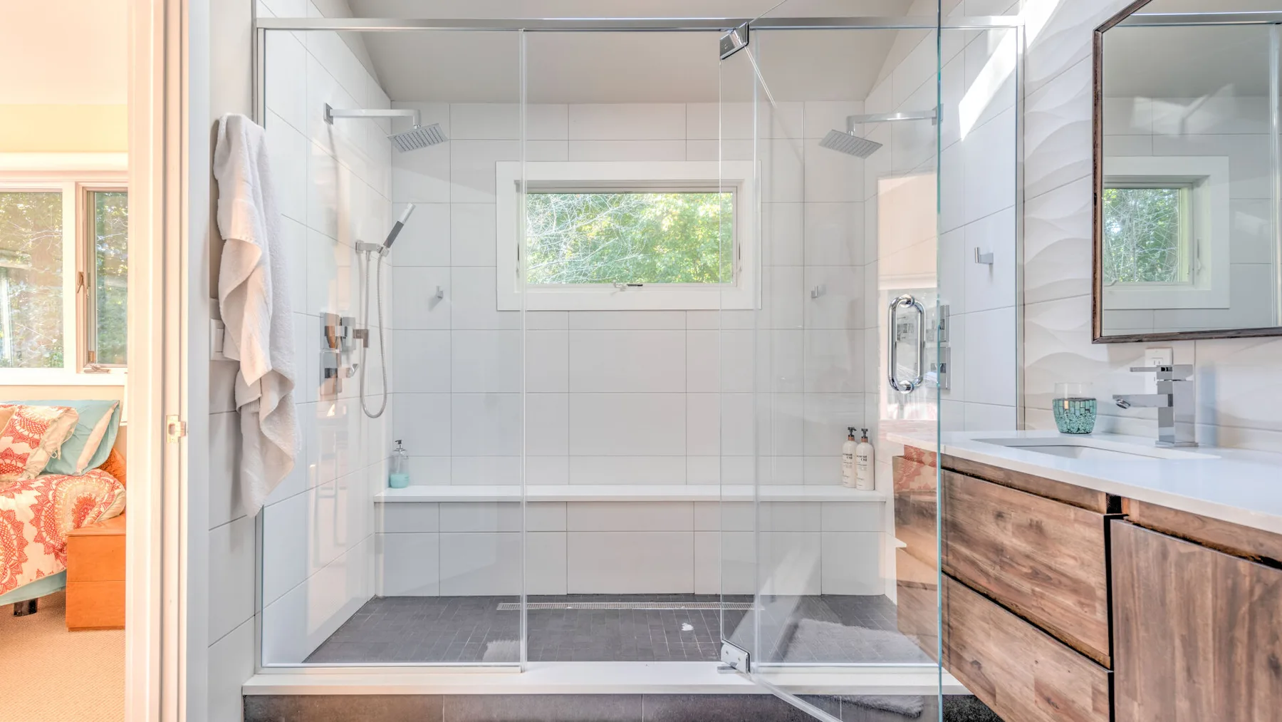 A bright bathroom with a glass shower, bathtub, and wood vanity.