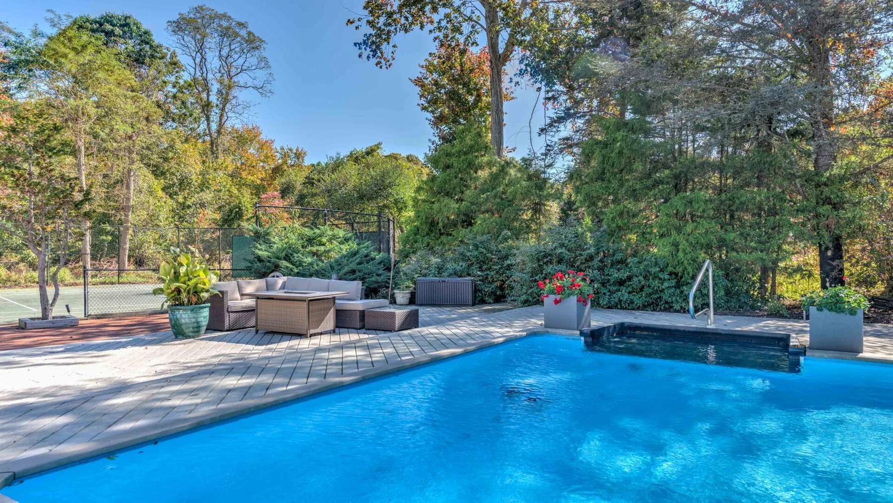 An outdoor swimming pool beside a paved deck and surrounding trees.