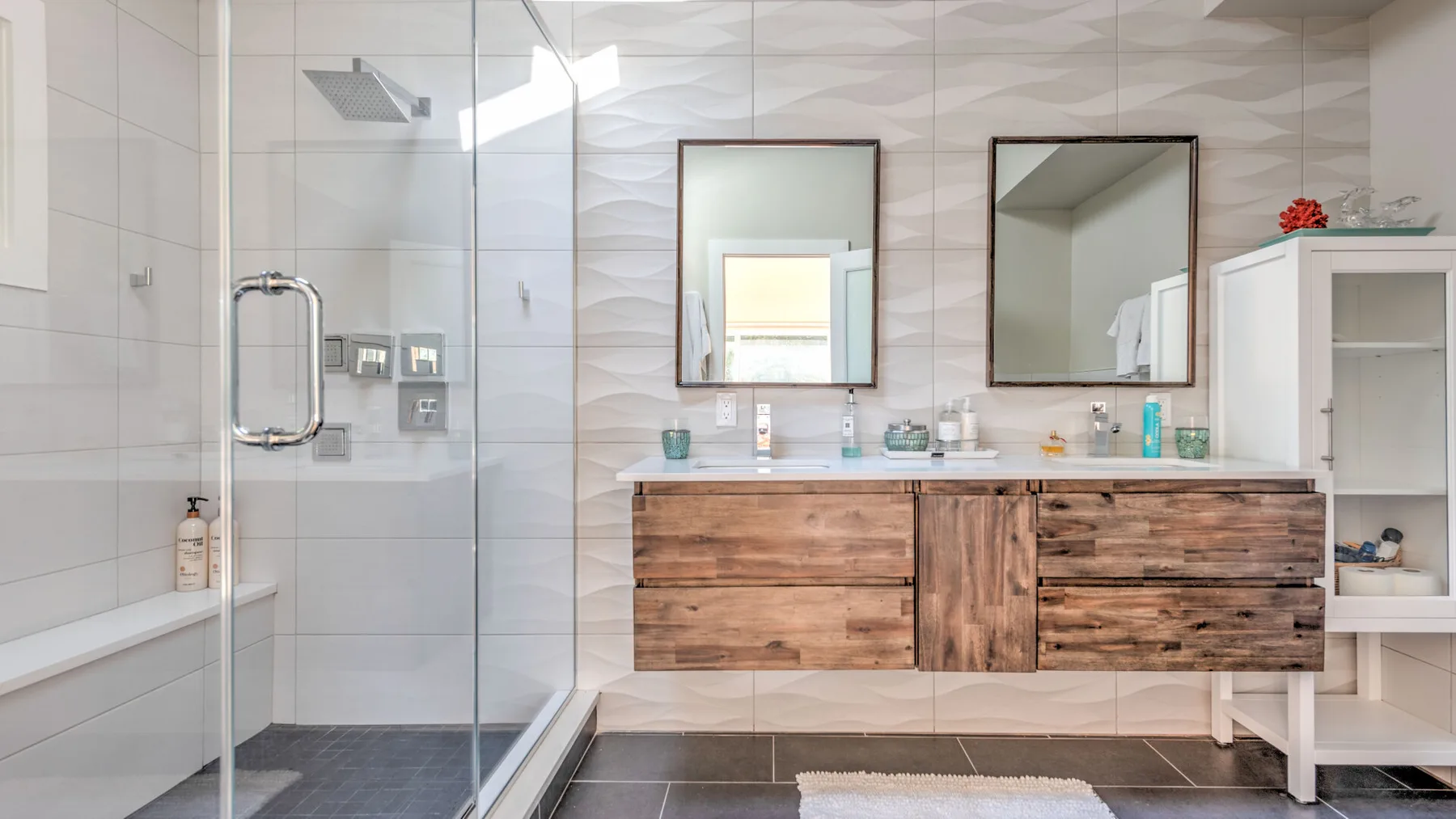 A bright bathroom with a glass shower, double vanity, and wall mirrors.