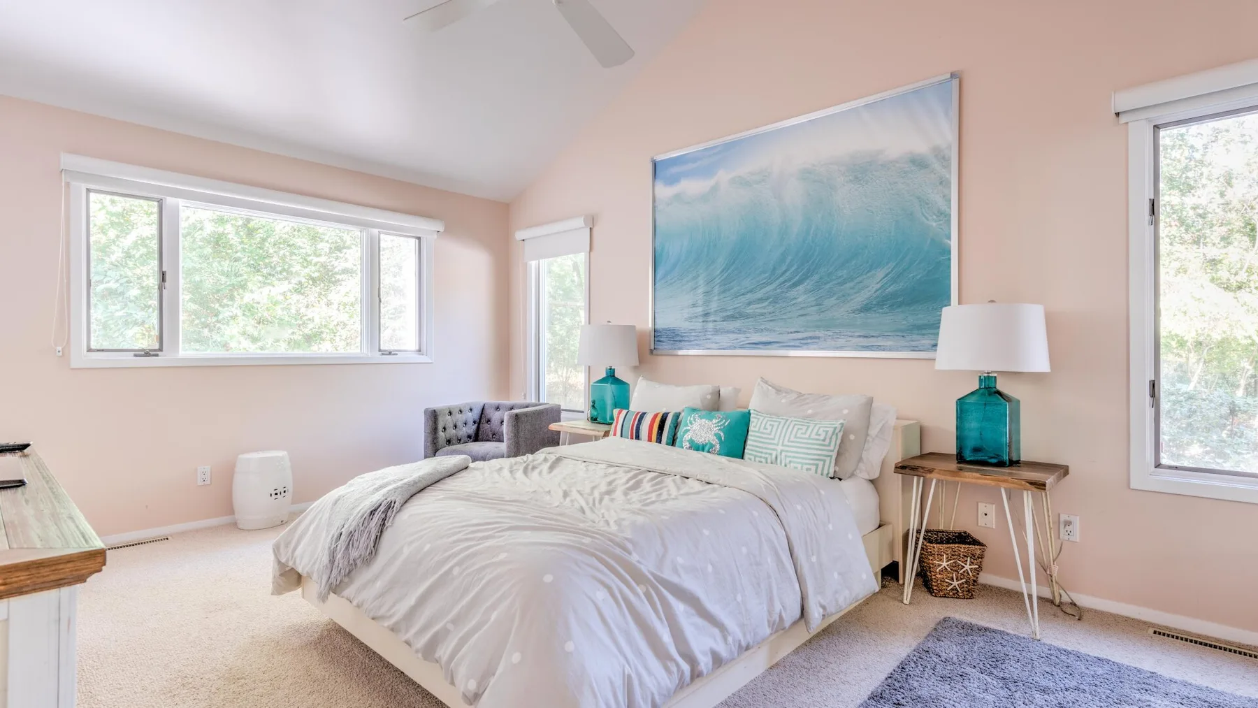 A bright bedroom features a bed beneath a large ocean-wave wall print.