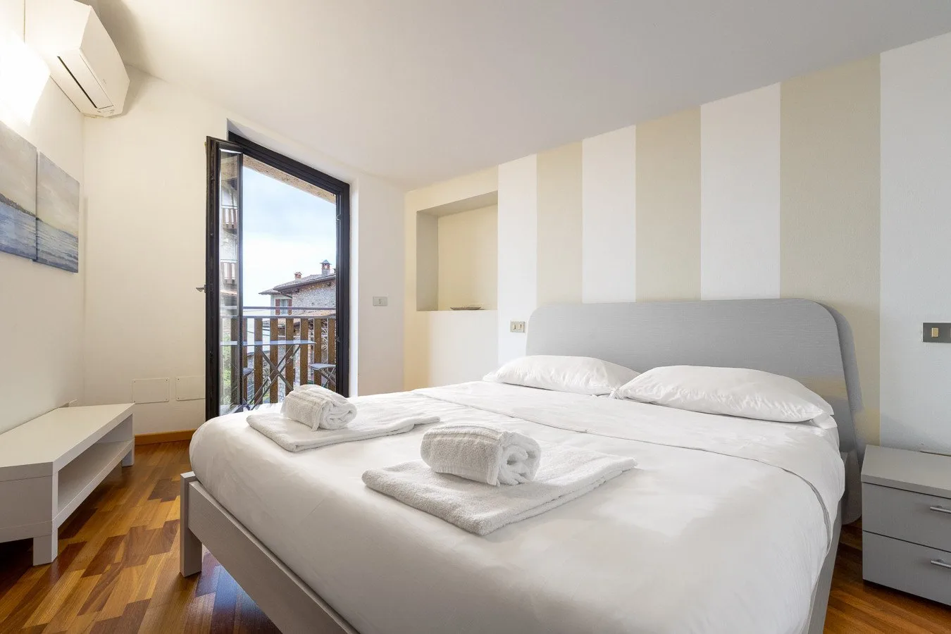 A bright bedroom with a neatly made bed and a glass door opening onto a balcony.