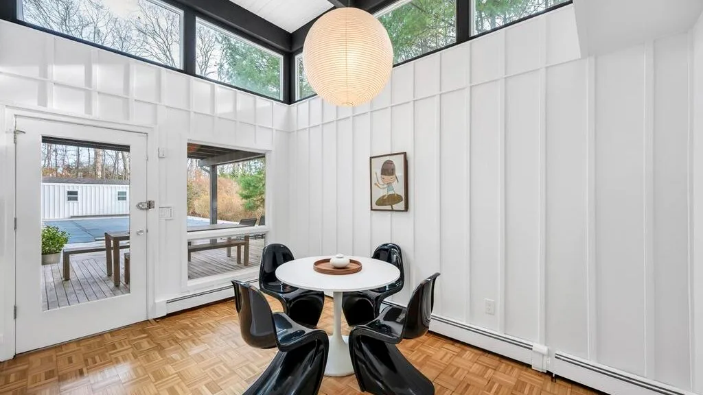 A bright dining area with a round table, dark seating, and tall windows.