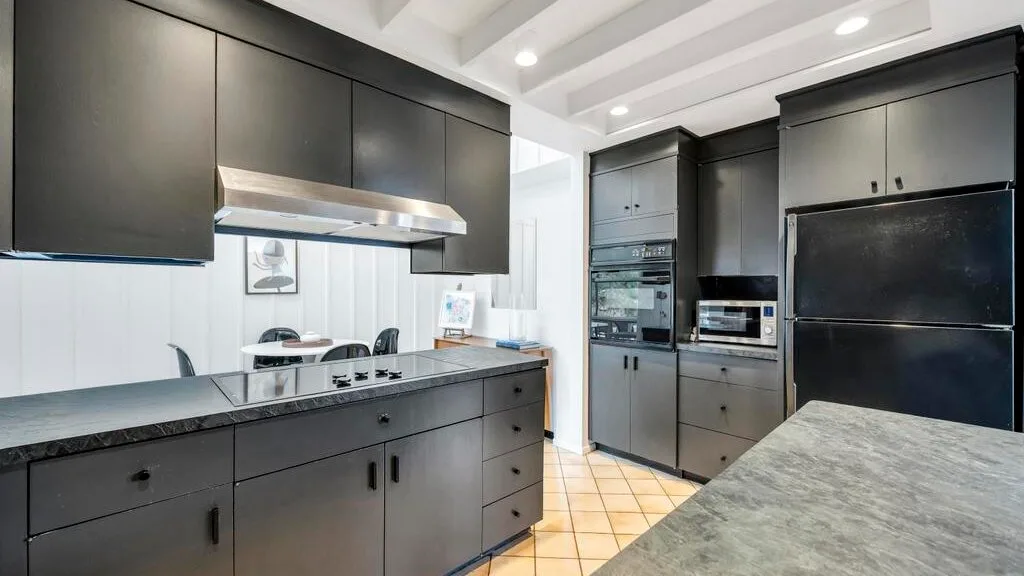 A modern kitchen with dark cabinetry, built-in appliances, and a wide island.