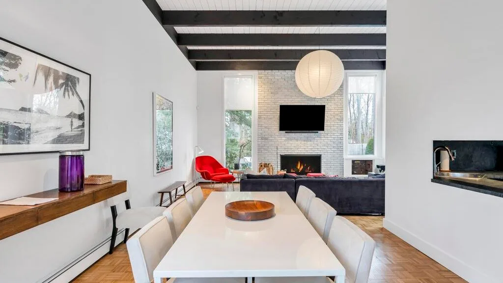 A dining area opens onto a living room with a fireplace and large windows.