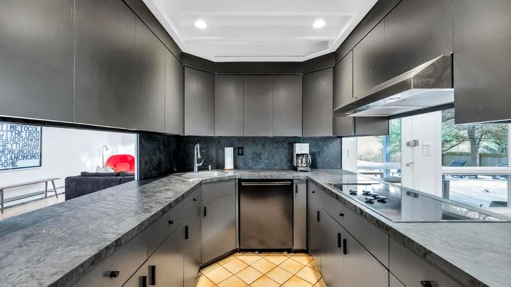 A modern kitchen with dark cabinetry, stone counters, and a central cooking area.