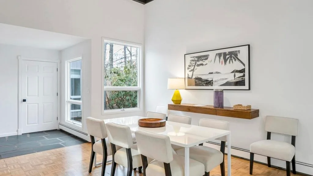 A bright dining area with a white table and chairs beside large windows.