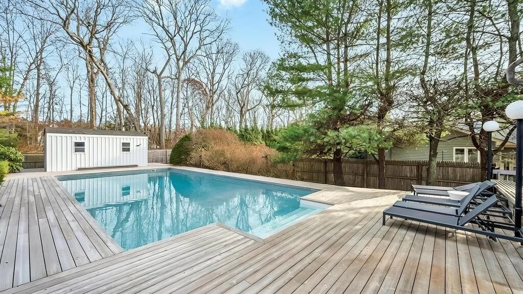 An outdoor swimming pool sits beside a spacious wooden deck and lounge seating.