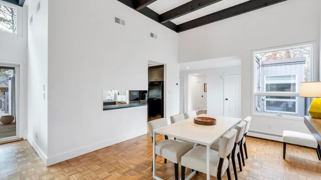A bright dining area features a table beneath dark exposed ceiling beams.