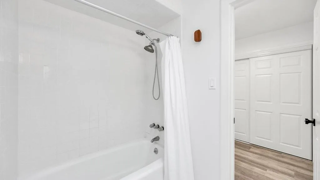A bathroom with a bathtub, shower, and white curtain.