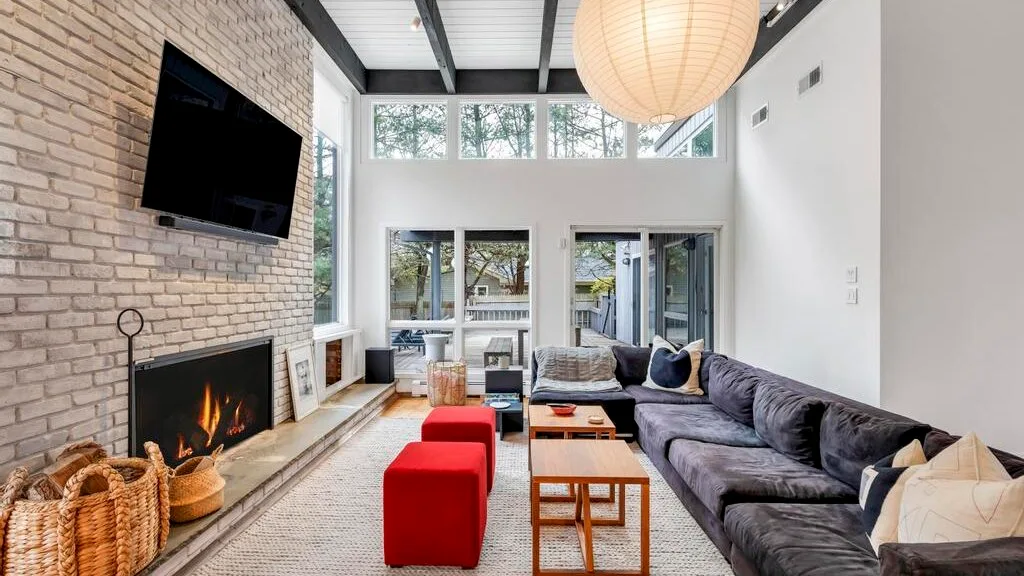 A bright living room with a sectional sofa, fireplace, and red ottomans.