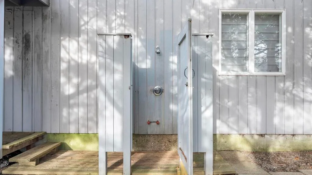 Exterior shower area with a shower fixture beside a window.