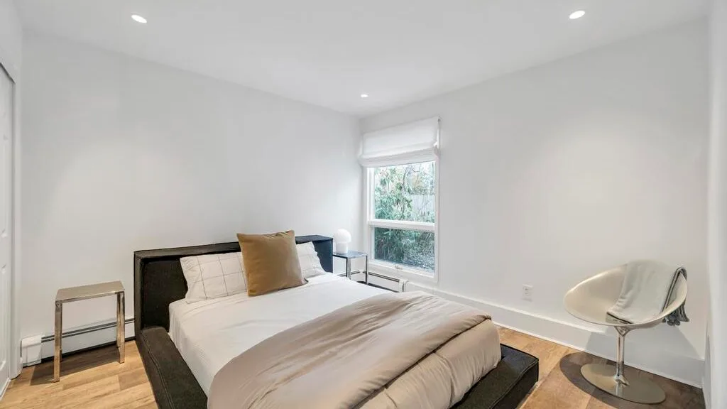 A bright bedroom with a bed beside a window and a small seating area.