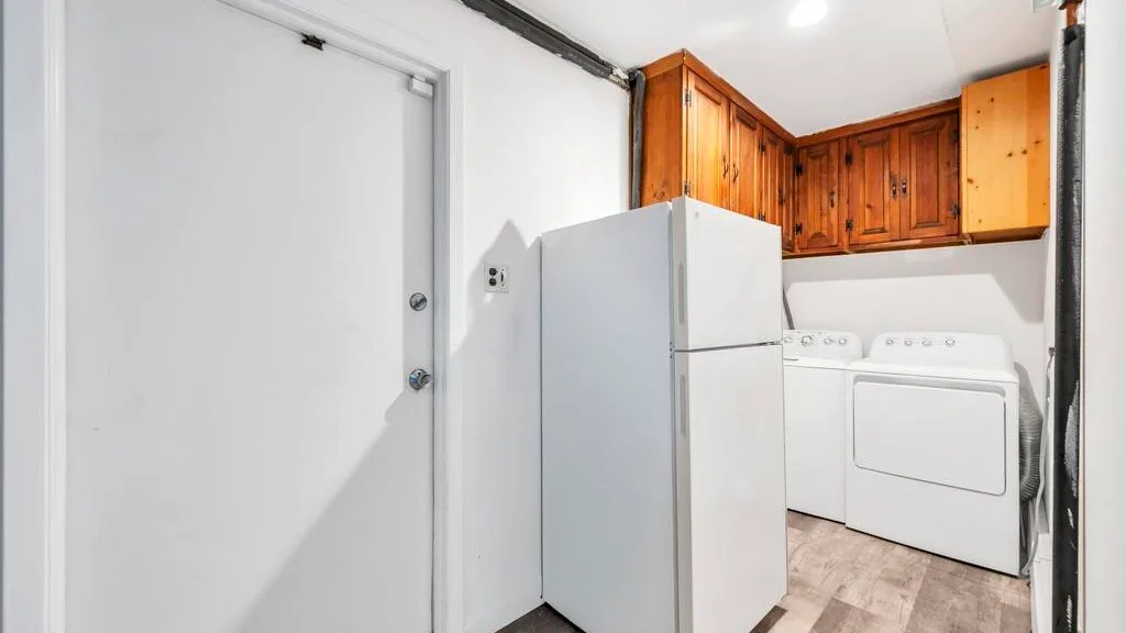 A laundry area with a refrigerator, washing machine, and wooden cabinets.
