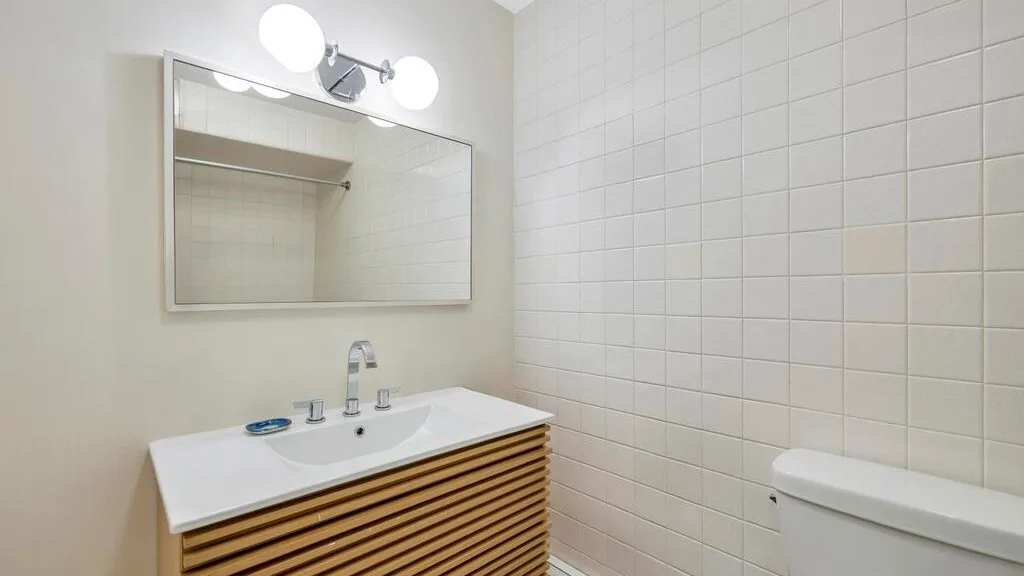 A bathroom vanity with a sink and mirror beside a tiled wall.
