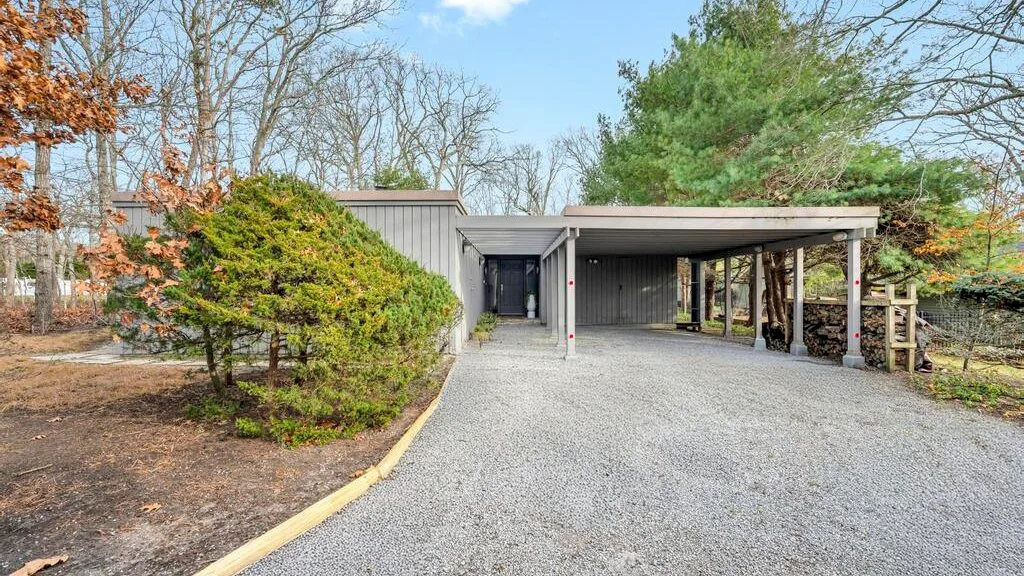 A gravel driveway leads to a covered parking area beside a low building.