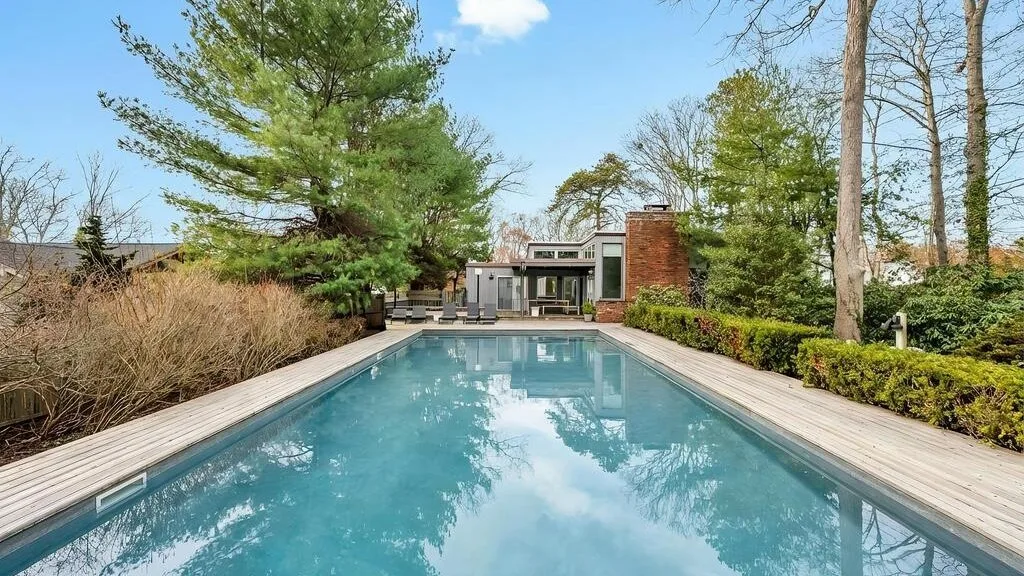 An outdoor swimming pool is surrounded by trees and a wooden deck.