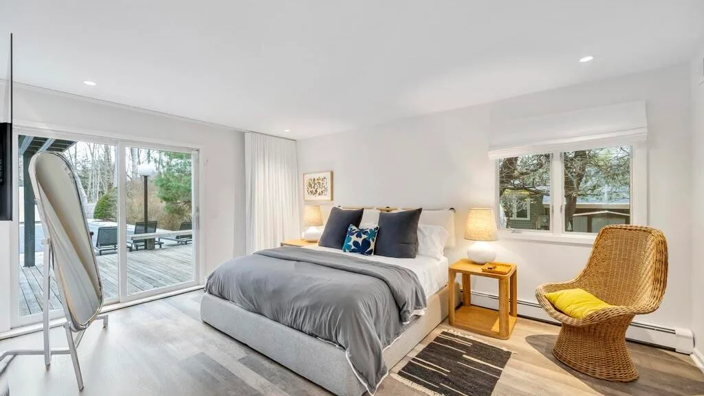 A bright bedroom with a bed, bedside table, and windows overlooking greenery.