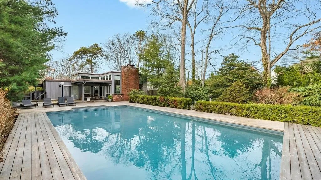 An outdoor swimming pool is surrounded by a wooden deck and landscaped greenery.