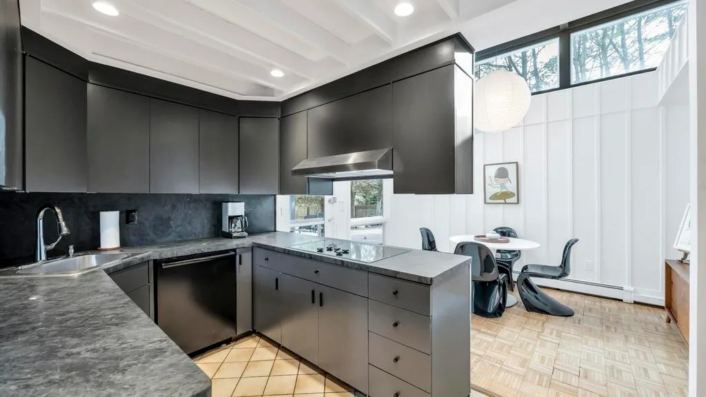 A modern kitchen with dark cabinetry, stone counters, and a bright dining area.