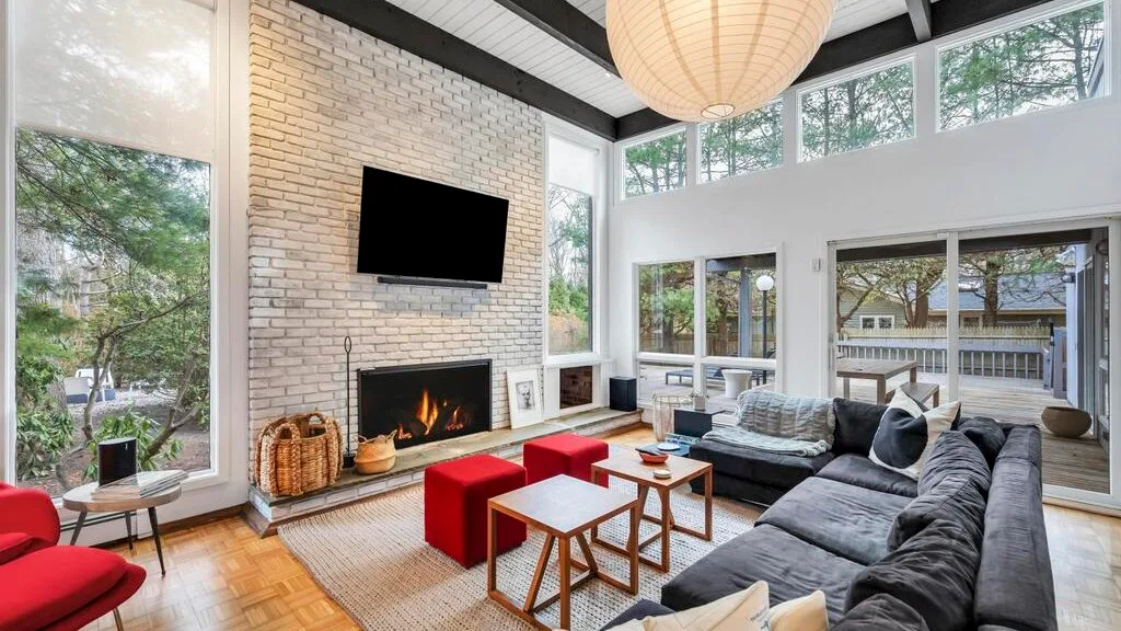A bright living room with a tall brick fireplace and seating around a coffee table.