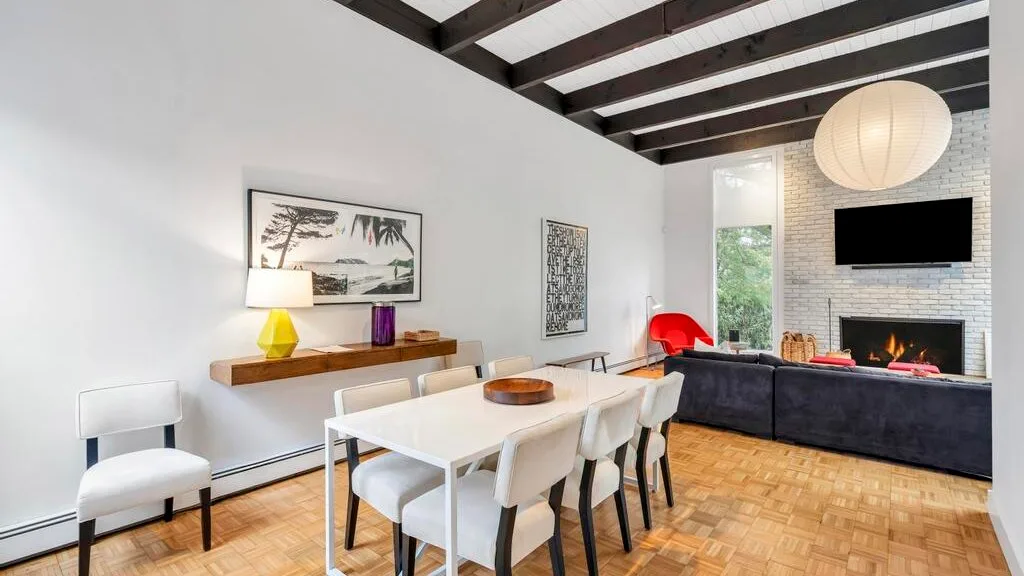 A dining area with a white table and chairs beside a living room with a fireplace.