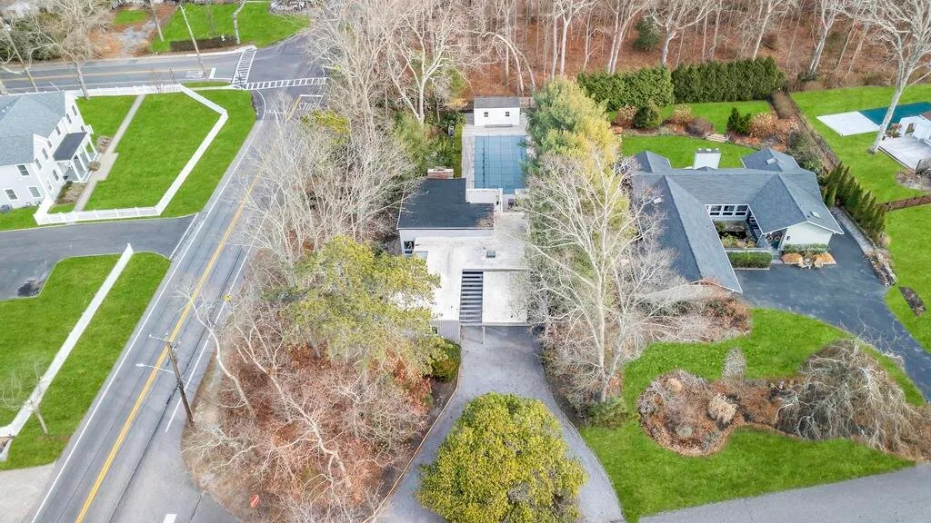 An aerial view shows a house, driveway, road, and surrounding trees.