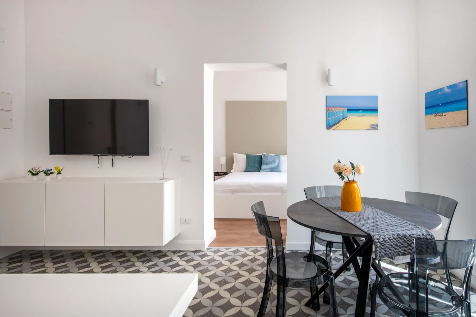 A bright dining area with a round table, beside a living room with a television.
