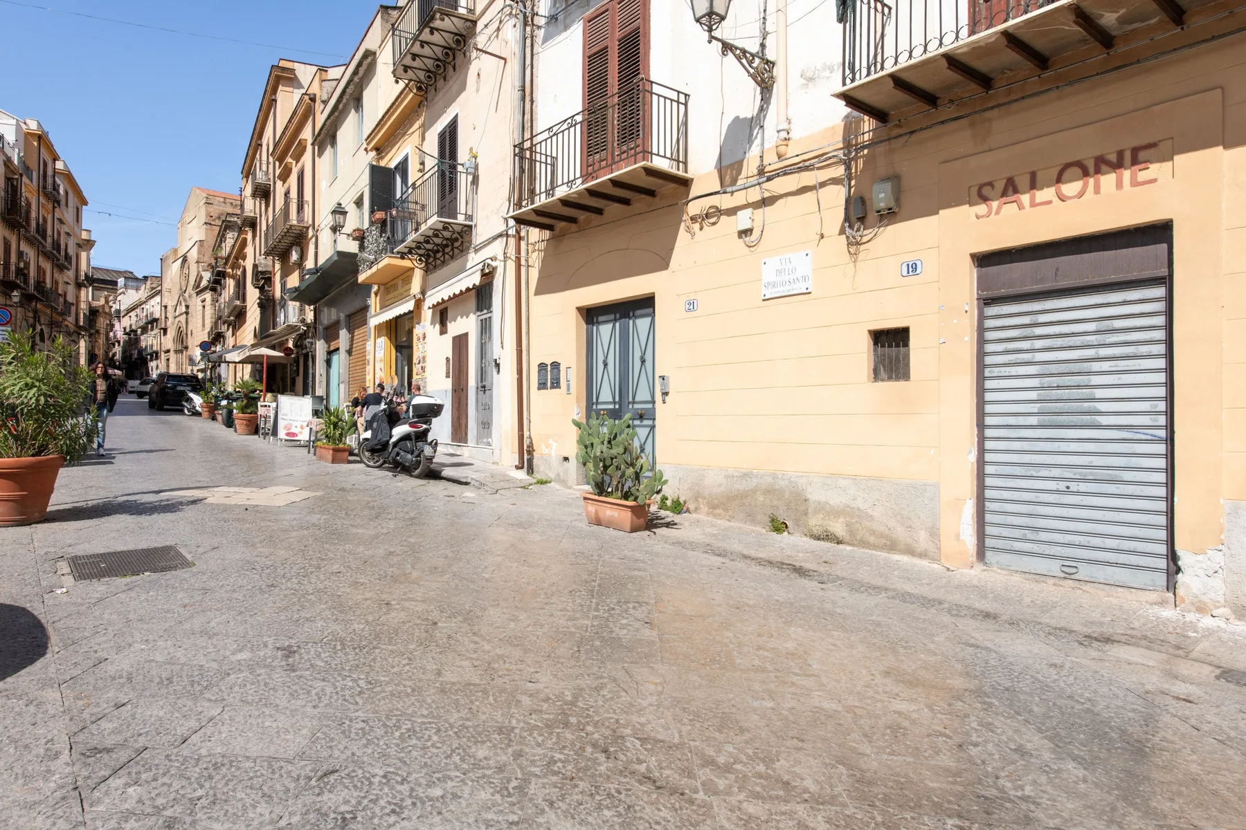 A narrow city street lined with attached buildings and parked scooters.