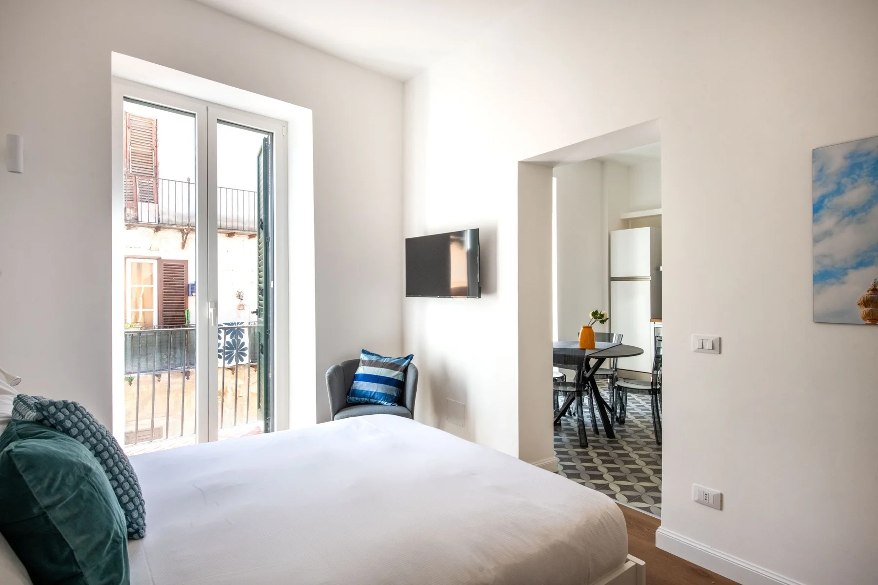 A bright bedroom with a bed beside tall glass doors and a small seating area.