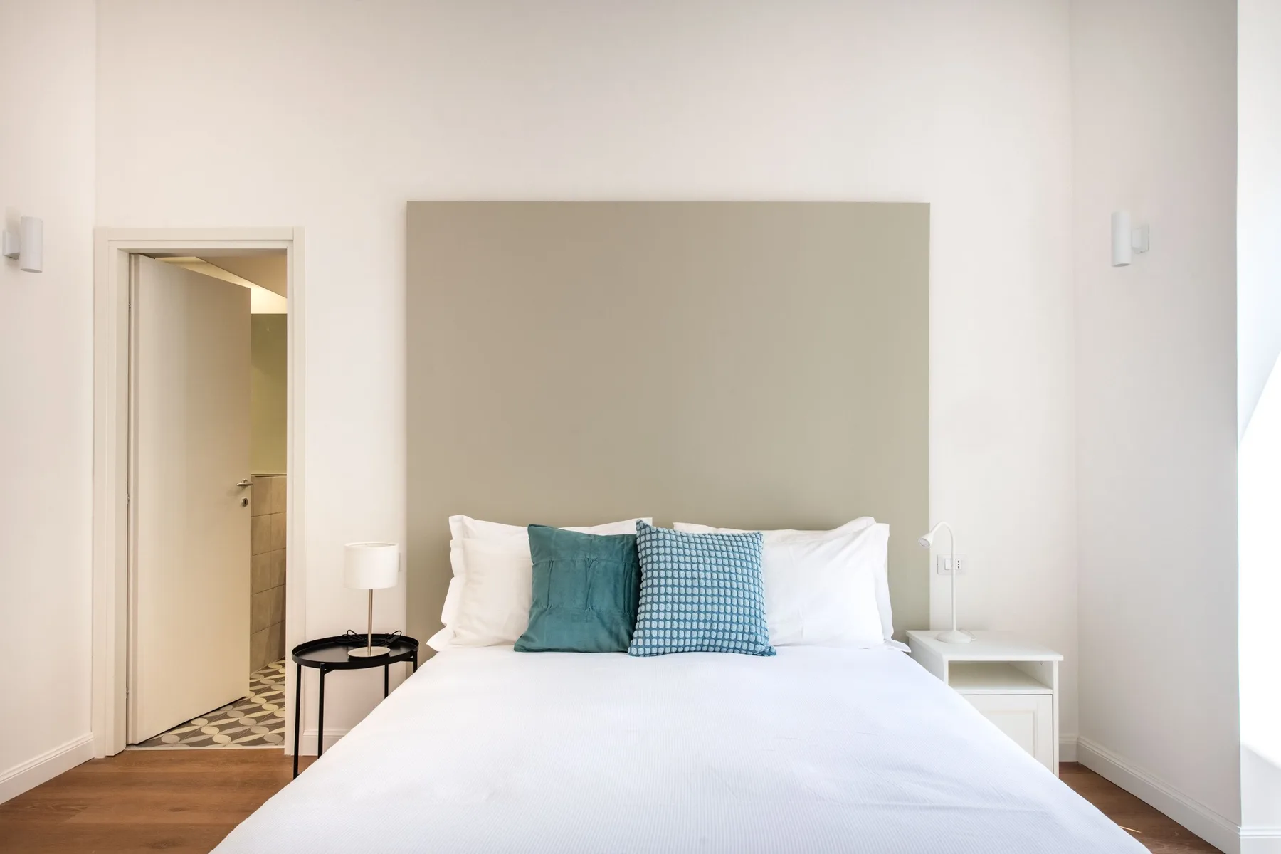 A bright bedroom with a neatly made bed and teal accent pillows.